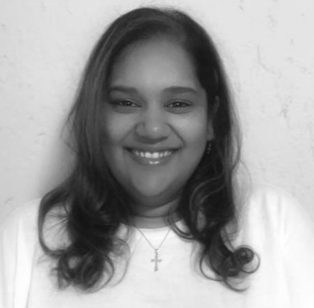 A woman wearing a white shirt and a cross necklace is smiling in a black and white photo.