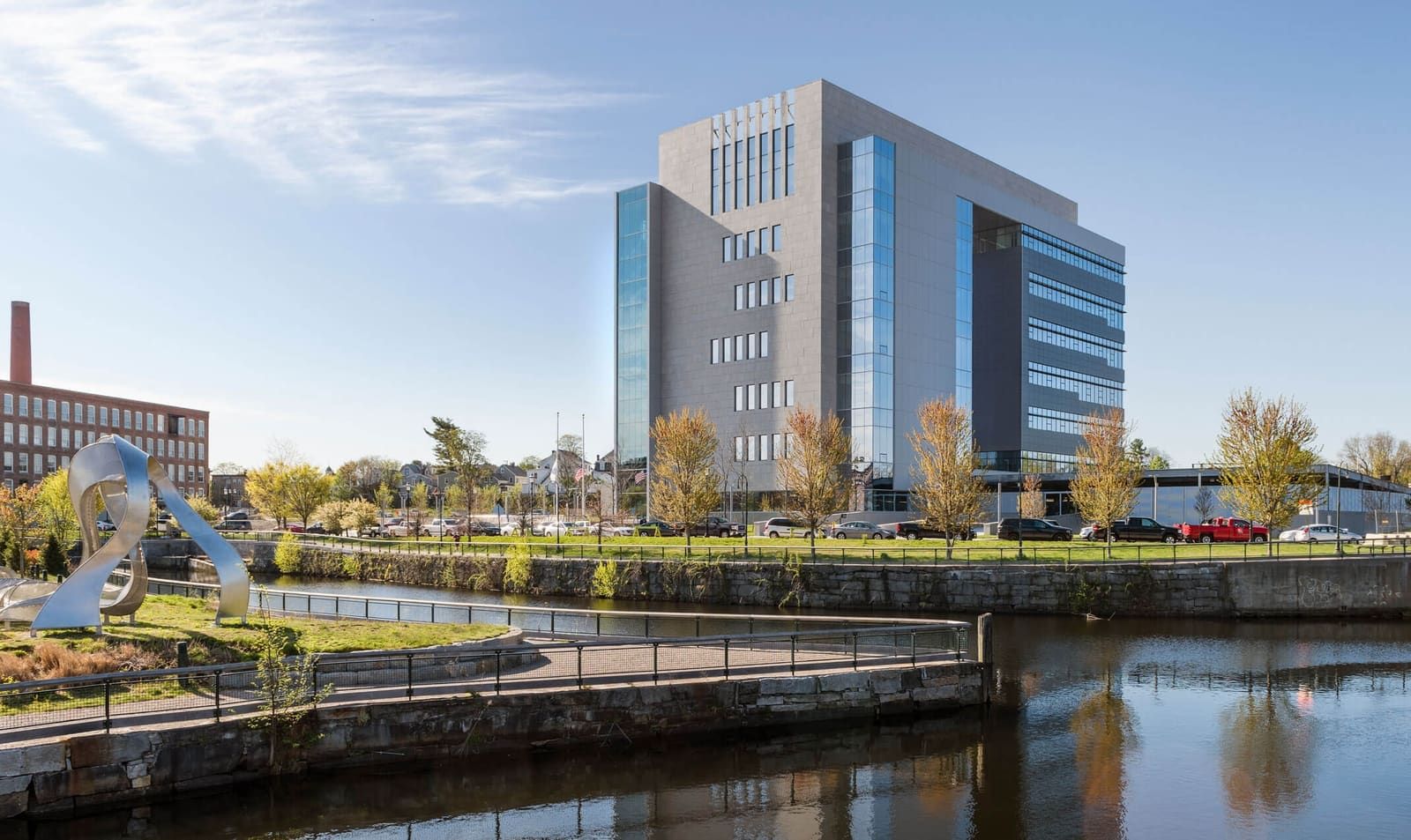 Modern office building beside a canal with trees and a blue sky