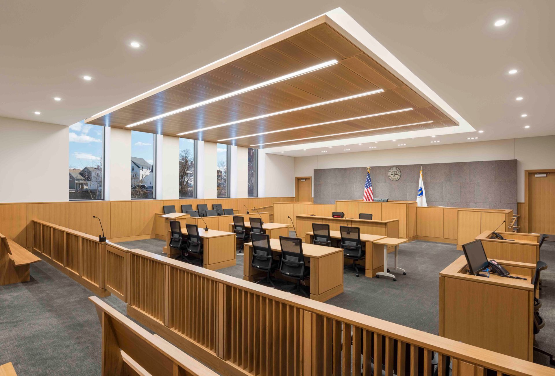 Empty modern courtroom with wood paneling, desks, flags, and angled ceiling lights