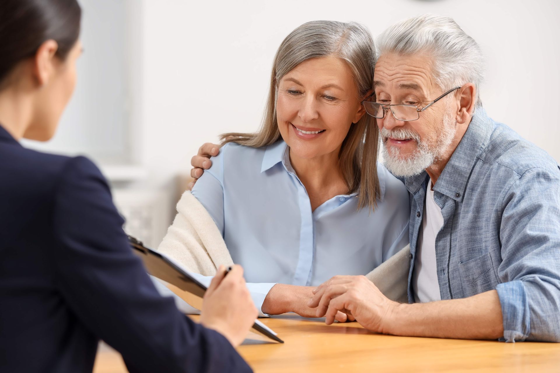 Couple speaking with a counselor at a desk, smiling and holding hands in a bright office.