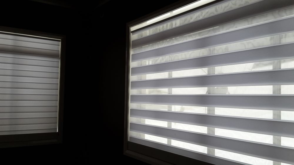 A Pair of Zebra Blinds on a Window in a Dark Room — Aussie Carpets & Vinyl In Beerwah, QLD