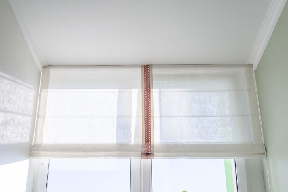 A White Roman Shade is Hanging Over a Window in a Room — Aussie Carpets & Vinyl In Buderim, QLD