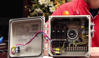 Open electronics enclosure with circuit board and wiring beside a red-shirted person