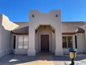 Sunlit adobe-style house exterior with a central wooden door and blue sky.