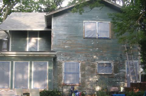 Two-story blue house with white trim, trees in front, and large windows on the lower level