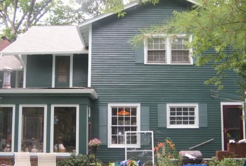 Two-story green house with white trim and a screened porch in a leafy yard