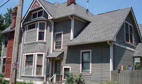 Gray Victorian house with bay windows and a steep roof, viewed from the street on a sunny day