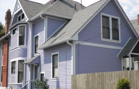 Lavender Victorian house with white trim and gray roof beside a wooden fence