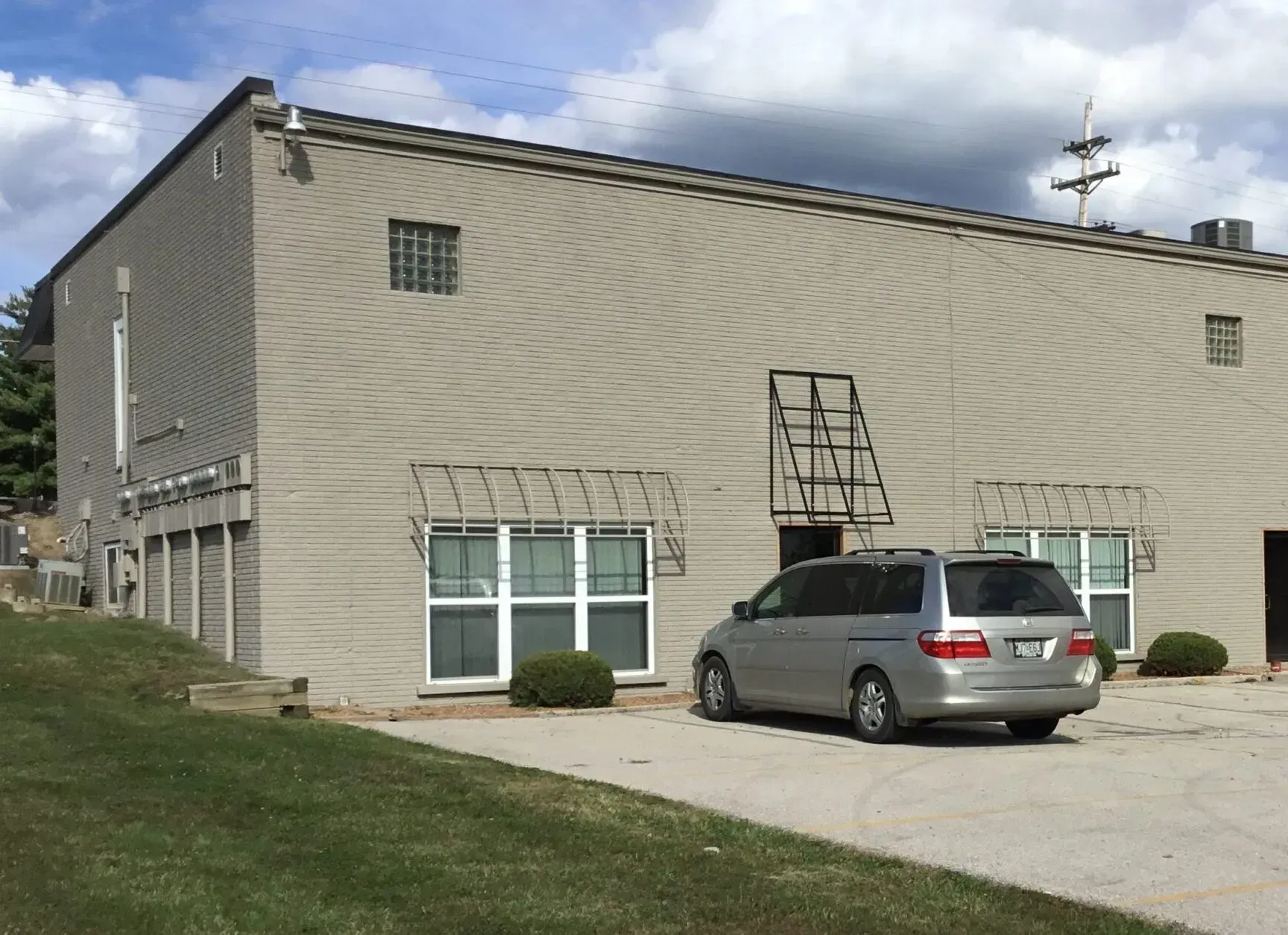 Beige building with windows and a silver minivan parked on a driveway under a cloudy sky