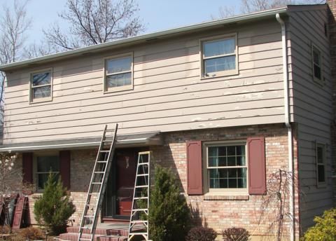 Two ladders leaning against a two-story beige house with red shutters and stone siding