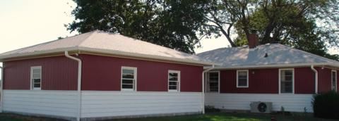 Red house with white trim and multiple windows, viewed from the front in a grassy yard.