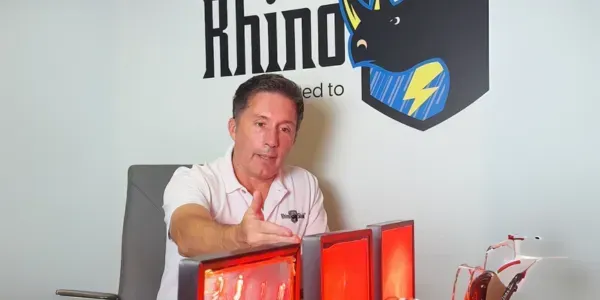 Man in white polo holding a clear shield beside glowing red and blue panels with Rhino logo backdrop
