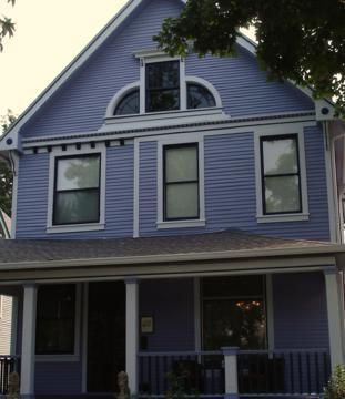 Blue Victorian-style house with white trim and a front porch under tree shade