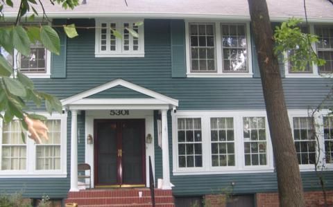 Two-story blue house with white trim, front porch, and red steps under trees
