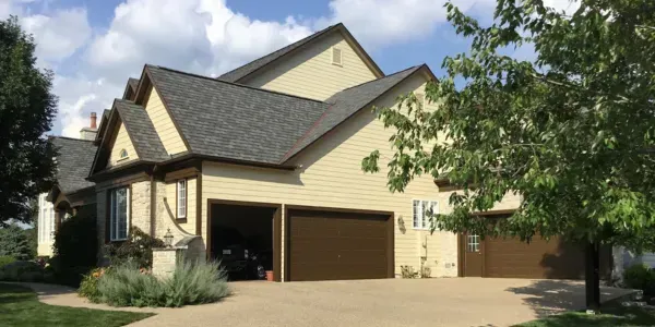 Suburban two-story beige house with brown garage doors and a tree in the front yard
