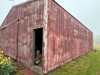 Weathered red wooden shed with an open doorway on a grassy field