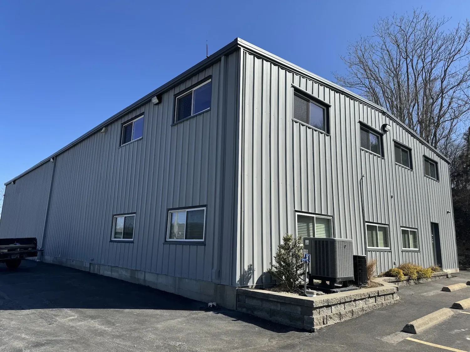 Gray metal-sided commercial building with windows, viewed from the parking lot on a sunny day