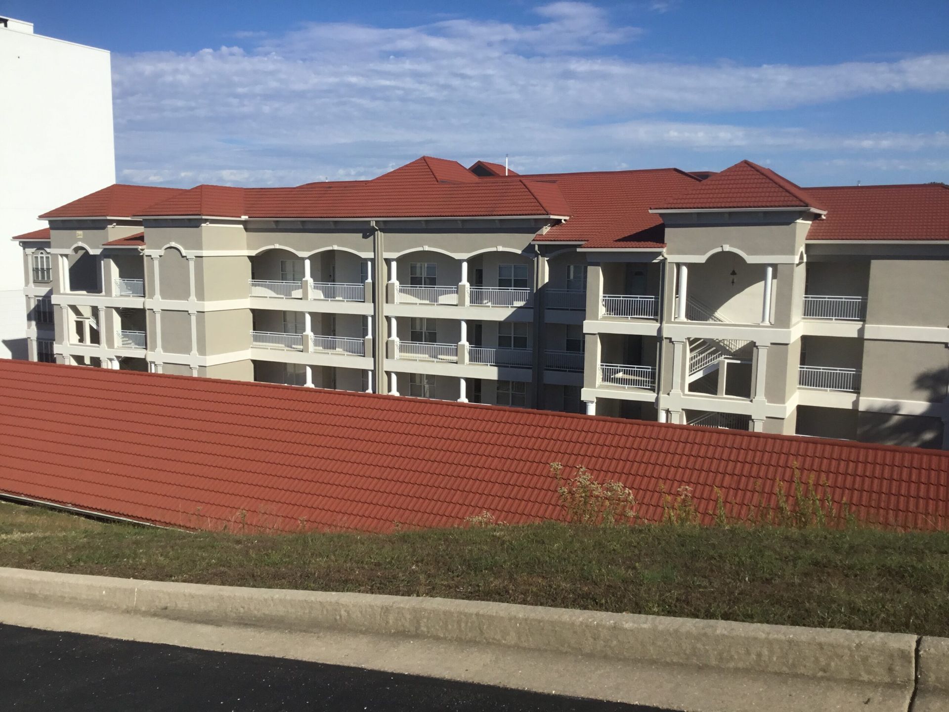 Apartment buildings with red roofs behind a red-tiled wall and grassy roadside curb