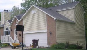 Suburban townhouse with beige siding, white garage door, brick accents, and a small front porch under overcast skies