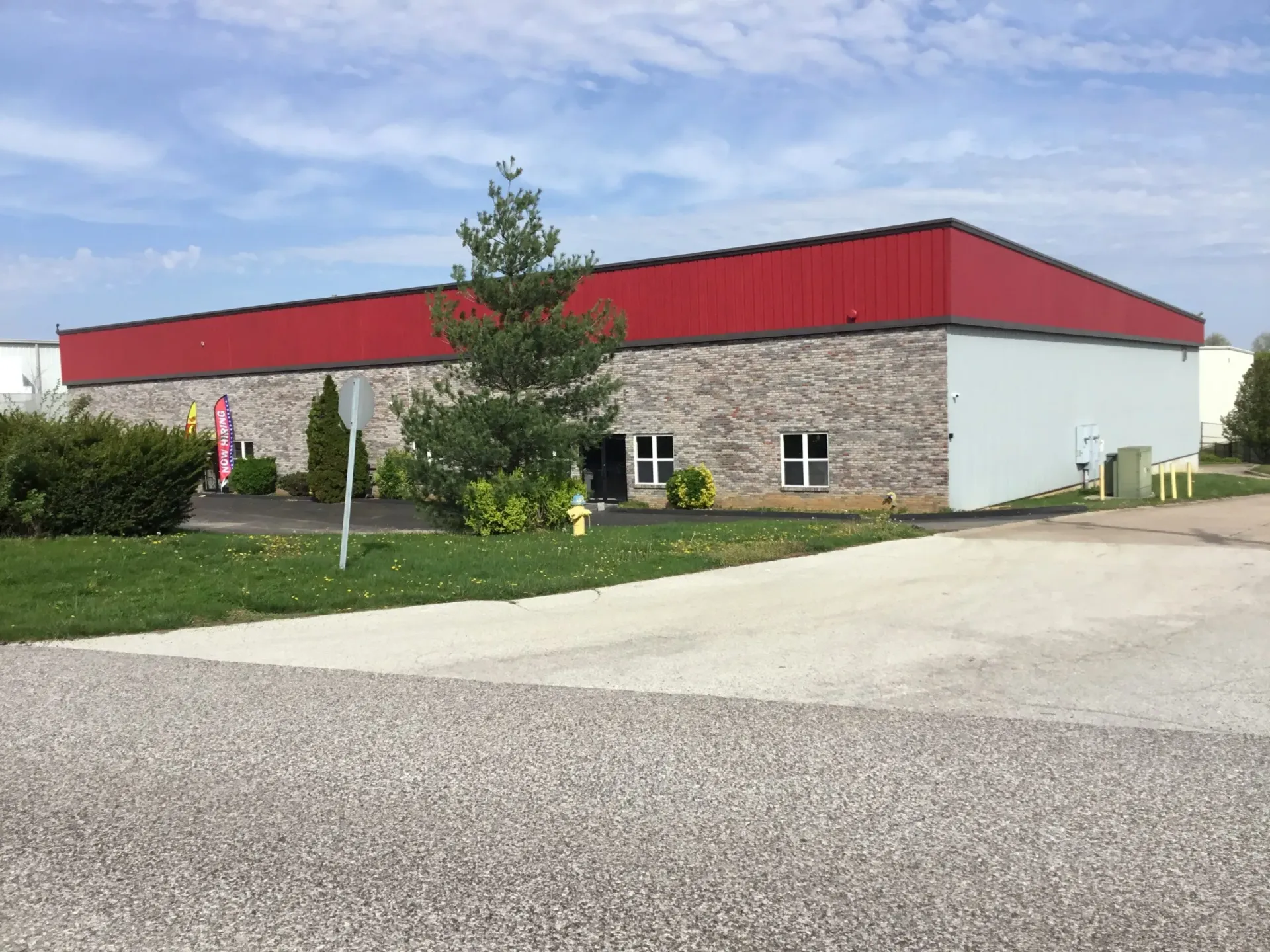 Single-story building with red roof and stone walls beside a gravel lot and green lawn