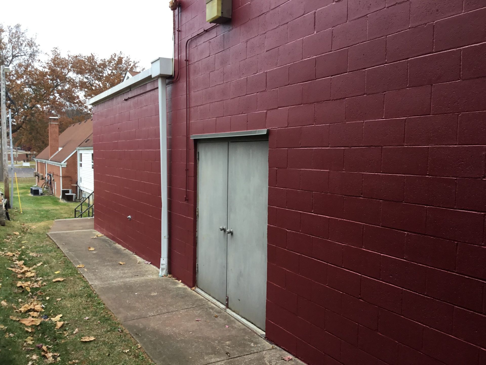 Maroon brick building with a gray double door and a sidewalk along the side.