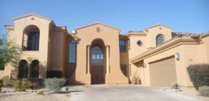 Beige stucco house exterior with arched windows and a central front entrance under a bright sky