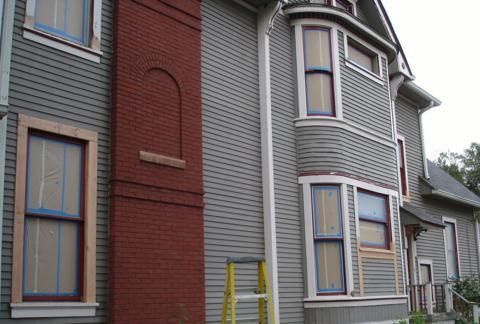 Row of houses with gray siding and a red brick wall, seen close up from the street.
