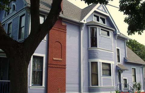 Two-story gray house with red brick chimney and white trim under a tree