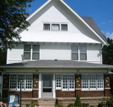 White two-story house with gray roof, front porch, and multiple windows under a blue sky