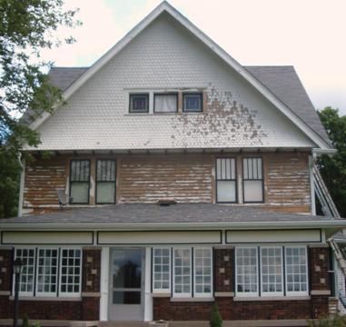 Two-story house with peeling white siding, brick lower level, and large front windows