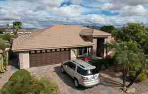 Suburban house with a tan roof, garage, and a silver SUV parked in the driveway.