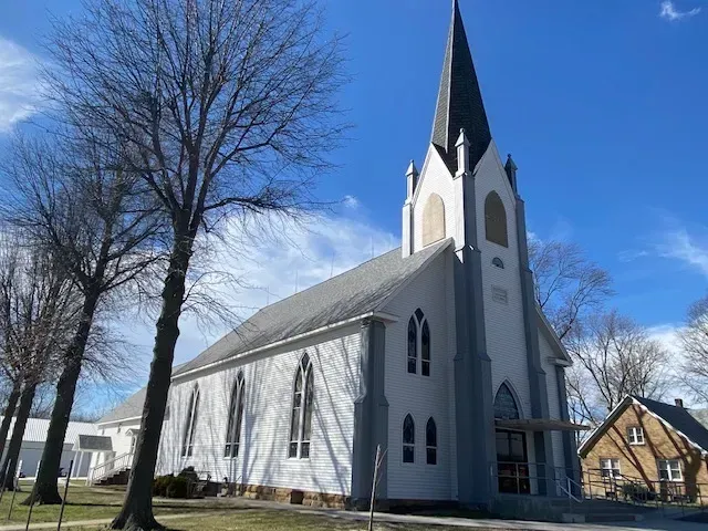 White church with tall steeple beside bare trees under a blue sky