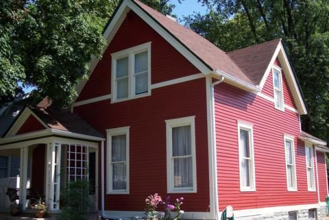Red house with white trim and front porch among trees