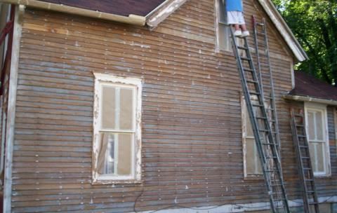 Old brown wooden house exterior with a ladder leaning against the wall near a window.