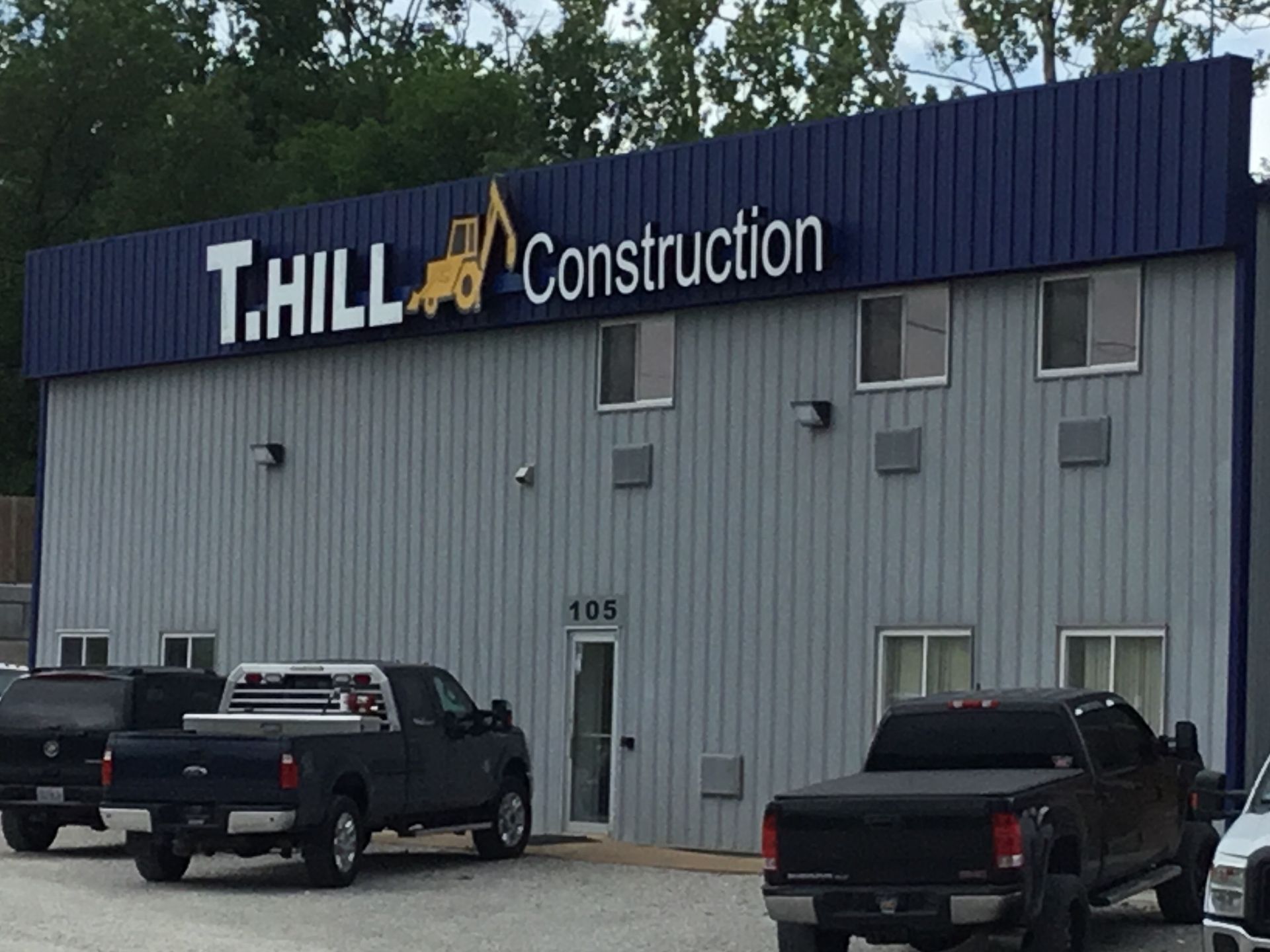 Thill Construction building with parked trucks in front and a gray exterior with blue sign