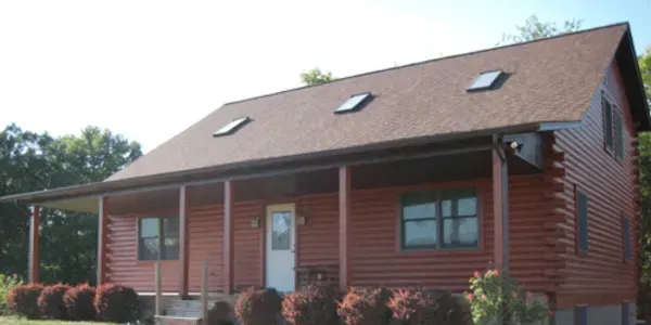 Red wooden house with a front porch, white door, and skylights on the roof