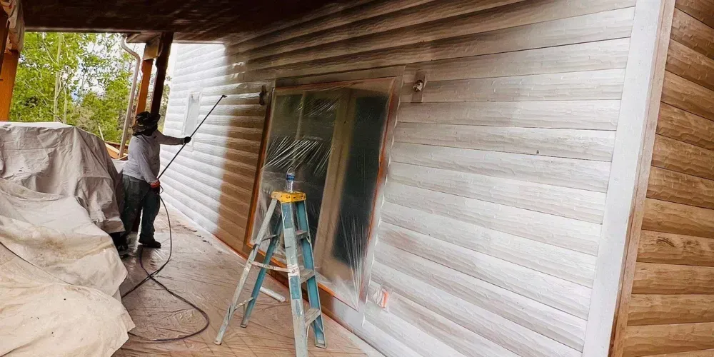 Worker on ladder painting exterior siding of a house under construction