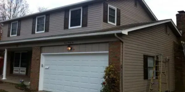 Two-story suburban house with beige siding, brick accents, and a white garage door