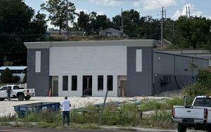 Small gray-and-white commercial building with parked trucks and a person standing in front