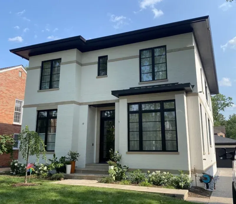 Modern two-story cream house with black trim, large windows, and a small front garden