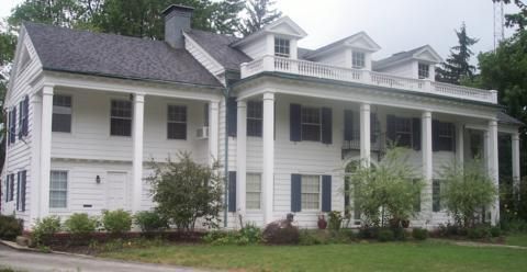 White two-story farmhouse with large columned porch, gray roof, and shrubs in front