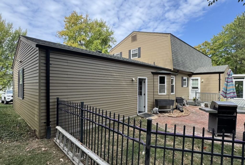 Exterior of a tan house with a fenced yard and brick patio under a cloudy sky