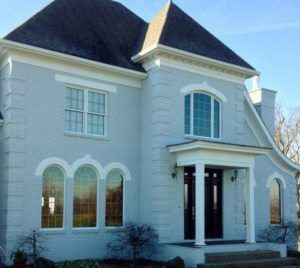 Large white two-story house with dark roof, arched windows, and front porch
