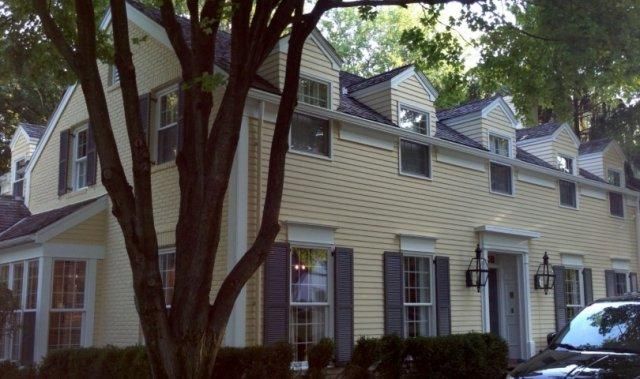 Row of cream-colored townhouses with dormer windows and trees in front, seen from the street