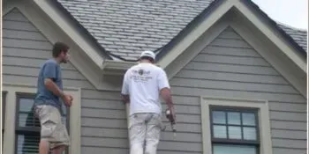 Two workers on a ladder repairing a house roof and siding