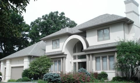 Large gray stucco home with an arched entry and landscaping