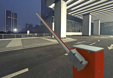 Barrera de estacionamiento roja y gris frente a un edificio de oficinas al anochecer.