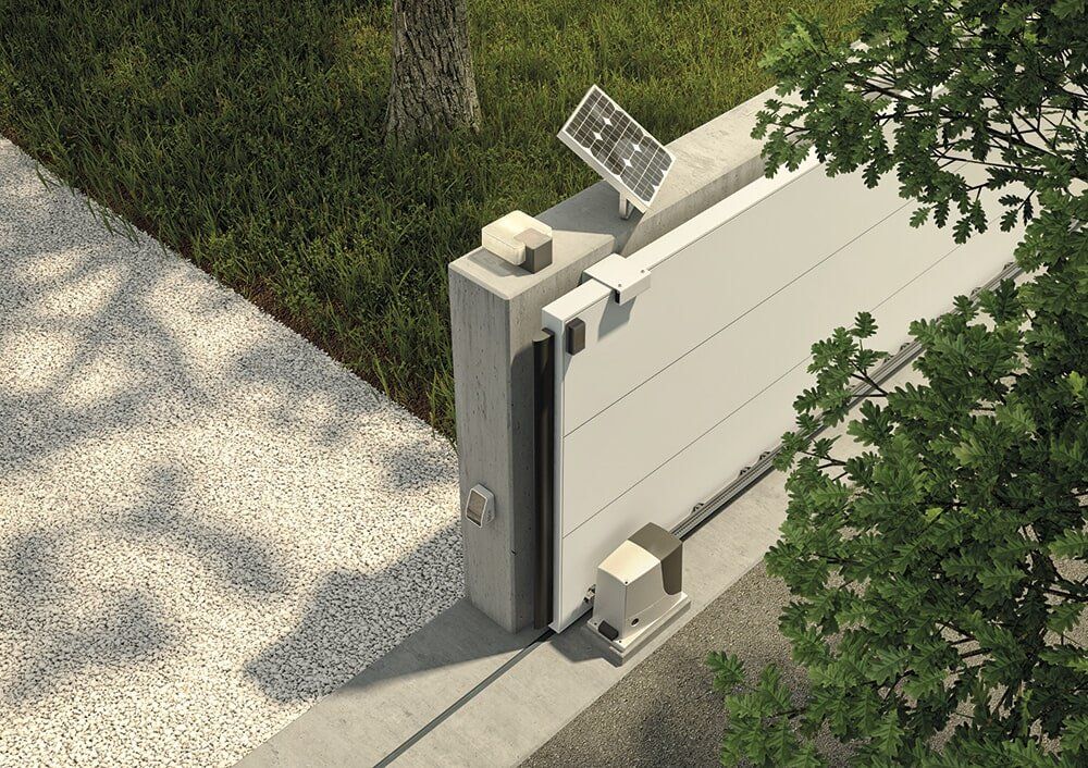 Puerta corrediza automática con panel solar sobre un pilar de hormigón al lado de un camino de grava y árboles.