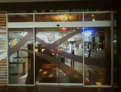 Puertas automáticas corredizas de vidrio con diseño gráfico decorativo, en entorno de centro comercial.