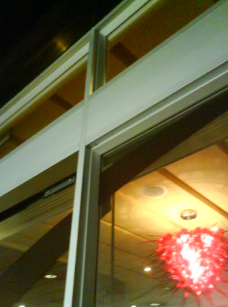 Detalle arquitectónico exterior: ventanas de vidrio, marco blanco, interior con luminaria roja e iluminación cálida.